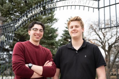 Photo of Nic Frello, student body president, and Caleb Jarvis, student body vice president standing next to each other in front of NDSU's main gates